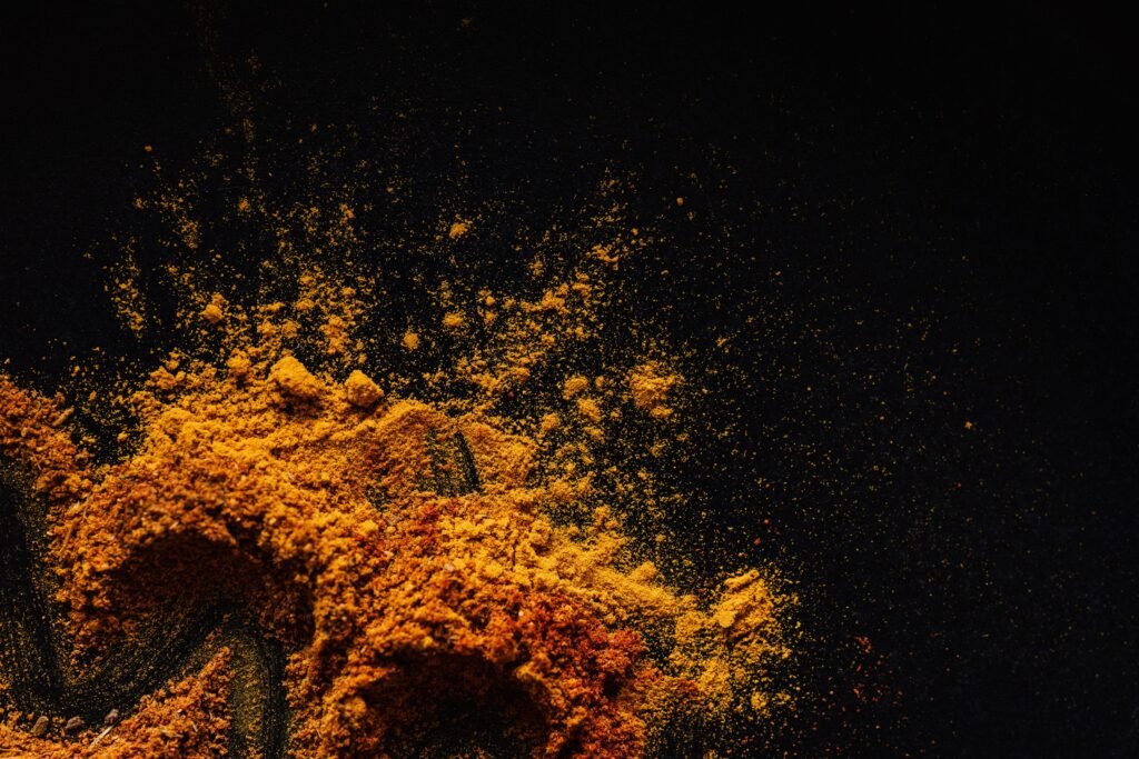 Ground turmeric and freshly cracked black pepper beside a healthy meal in a kitchen