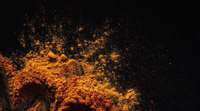 Ground turmeric and freshly cracked black pepper beside a healthy meal in a kitchen