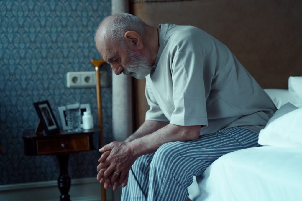 Older adult awake in bed at night looking at a bedside clock, illustrating difficulty staying asleep.