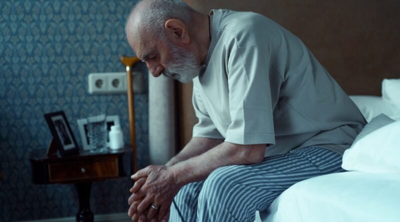 Older adult awake in bed at night looking at a bedside clock, illustrating difficulty staying asleep.